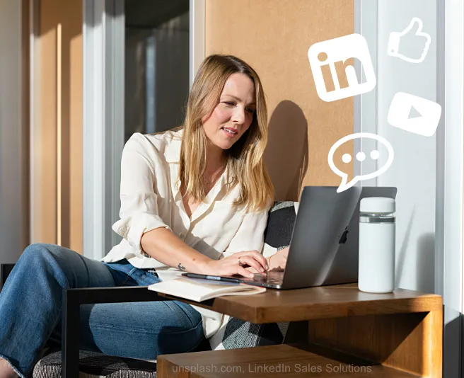 Frau in Langarmhemd und Jeans sitzt an Holztisch mit Laptop und bedient Social Media